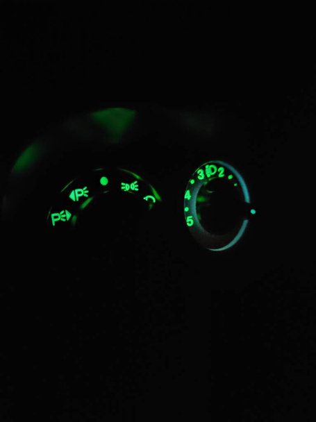 Panel verde brillante en el coche en la oscuridad, en el panel hay un interruptor de estacionamiento, luces de estacionamiento, haz alto y bajo. - Foto, Imagen
