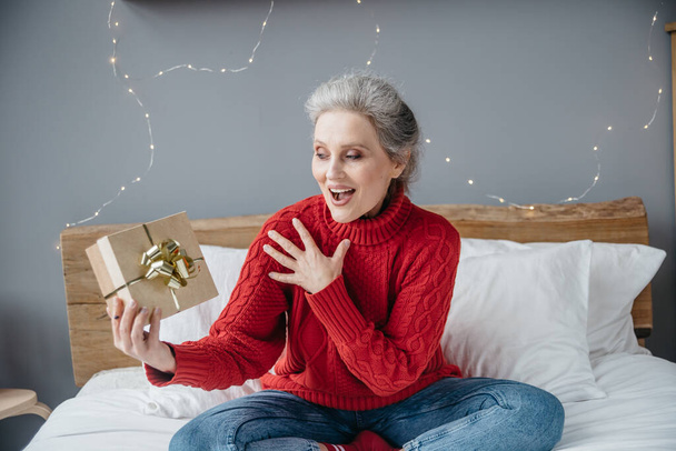 クリスマスライトの背景に家で贈り物と美しい感情的なシニア女性 - 写真・画像