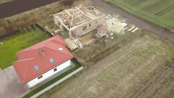 Top down aerial view of two private houses, one under construction with wooden roofing frame and another finished with red tiled roof. - Footage, Video