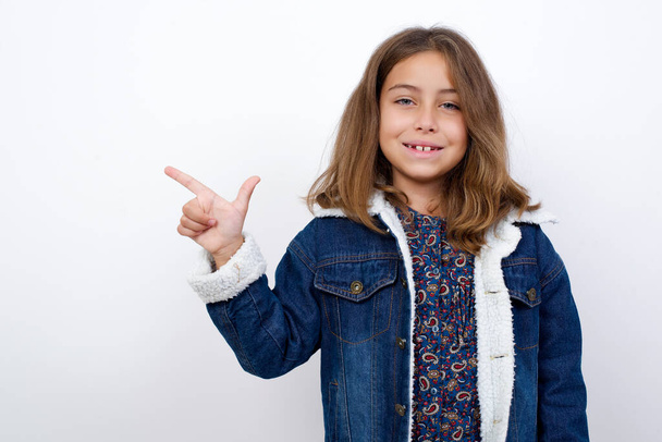 Little caucasian girl with beautiful blue eyes wearing denim jacket standing over isolated white background pointing up with fingers number eight in Chinese sign language B. - Fotografie, Obrázek