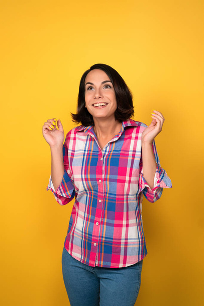 Hilarious young woman raised her hands up and smiled on yellow background - Photo, image
