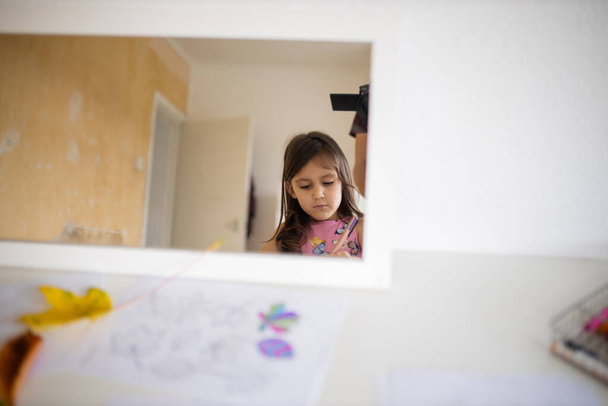 Καθρέφτης σε λευκό τραπέζι που αντανακλά ένα μικρό κορίτσι και μια λευκή ανοιχτή πόρτα - Φωτογραφία, εικόνα