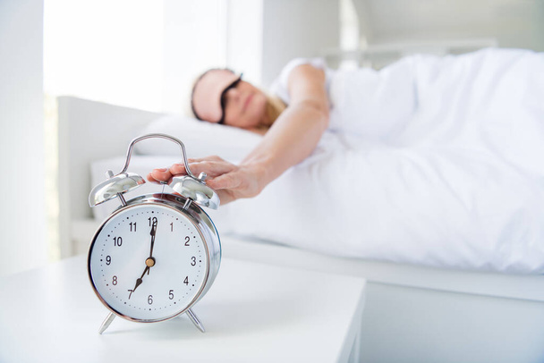 Photo of aged lady woman lying sleeping bed white sheets turn off metal alarm clock ring seven oclock bedroom indoors - Фото, зображення