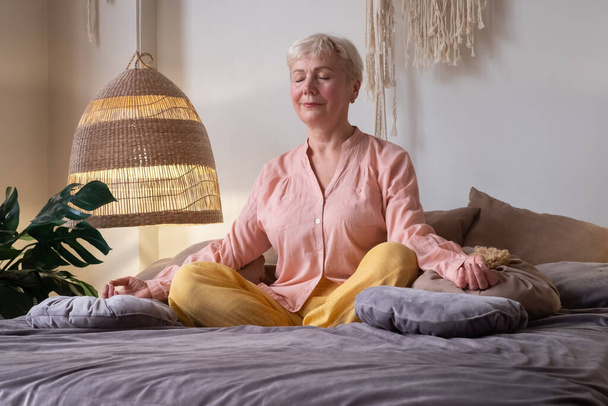 Starsza kaukaska kobieta medytuje praktykując jogę w pomieszczeniach. - Zdjęcie, obraz