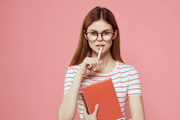 жінка-студент з блокнотами на рожевому фоні жестикулює руками окуляри на її обличчі смугаста футболка модель
 - Фото, зображення