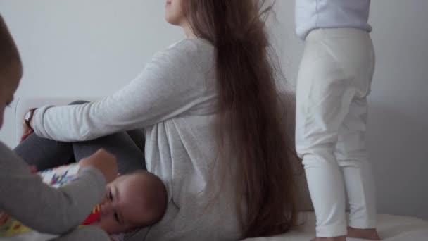 Childhood, motherhood, siblings concept - Carefree young mum combs her little kid daughter hair , son and newborn baby have fun play on bed, happy cheerful family laugh tickles, kiss, hugs lying relax - Footage, Video