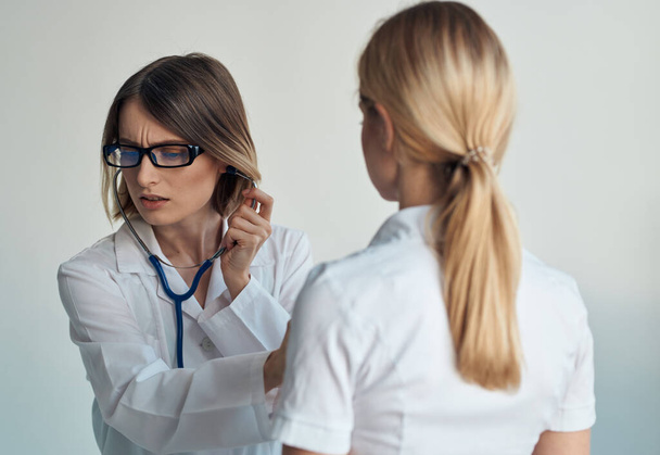 Der Arzt hört den Herzschlag des Patienten durch ein Stethoskop auf hellem Hintergrund - Foto, Bild