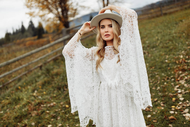Adorable woman posing at the field, wearing gorgeous lace dress and white hat, beautiful lady looking at the camera, send out tenderness and women charm, girl beauty concept - Foto, Imagem