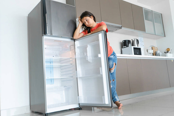 The girl is surprised at the empty refrigerator. Lack of food. Food delivery. - 写真・画像