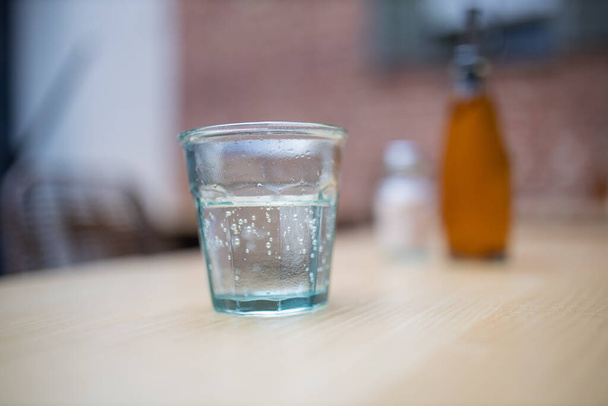 Glass of water on a wooden table with blurry bottles as background - 写真・画像