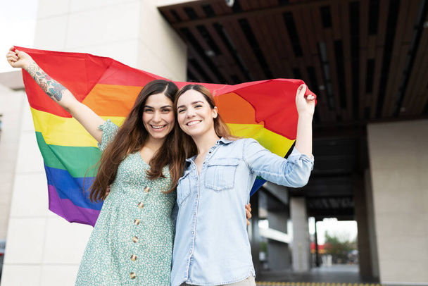 Zwei hübsche junge Freundinnen mit einer Regenbogenfahne in der Hand zur Unterstützung der LGBT-Rechte - Foto, Bild
