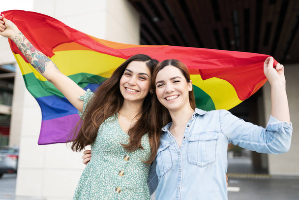 Feliz pareja lesbiana ondeando una bandera arco iris orgullo gay en apoyo de los derechos LGBT  - Foto, Imagen