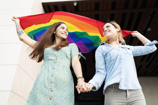 Gay couple looking happy face to face with a fluttering gay pride rainbow flag above their heads - Fotoğraf, Görsel