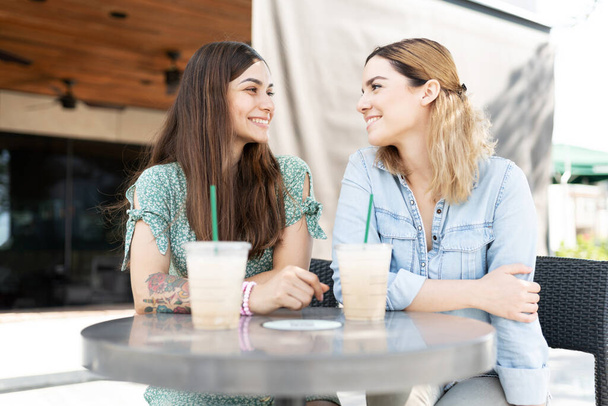 Две девушки-геи, выглядящие счастливыми фейри лицом к лицу и сидящие во внутреннем дворике кафе - Фото, изображение