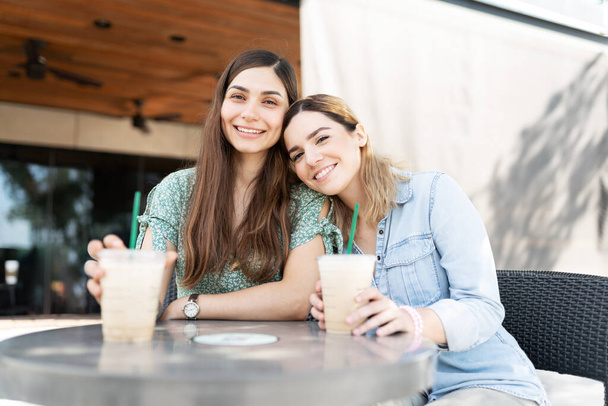 Kaukasische junge Frau lächelt und legt ihren Kopf in die Schulter ihres lateinischen Freundes, während sie Kaffee trinkt - Foto, Bild
