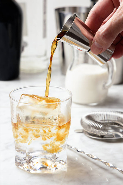 Adamın eli buzlu bir bardağa kahve likörü döküyor. Beyaz Rus kokteyl hazırlığı - Fotoğraf, Görsel