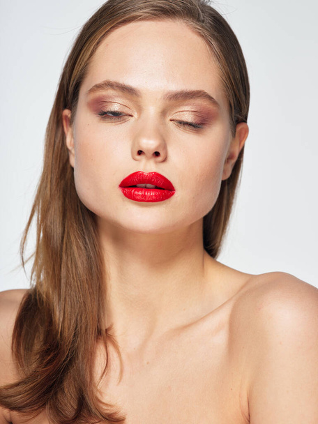 Een vrouw met blote schouders scheert haar ogen rood lippenstift ja een grijze achtergrond  - Foto, afbeelding