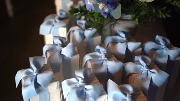 Ortasında çiçek buketi olan ziyafet masasında güzel hediyeler, vaftiz partisi için hazırlanmış mavi kurdeleli küçük beyaz karton kutular. Bonniere kutularının içindeki tatlı konfeti, minnettar. - Video, Çekim