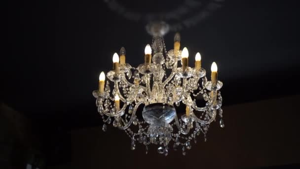 Enorme kristallen kroonluchter hangend aan huisplafond in donkere kamer, mooie vintage kroonluchter met diamanten details en LED lampjes in kandelaar. Lichtgevende kristallen lamp op plafond - Video