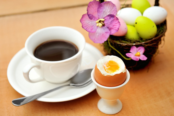 Värikäs maalattu pääsiäismunia korissa, kuppi mustaa kahvia ja munakuppia
 - Valokuva, kuva