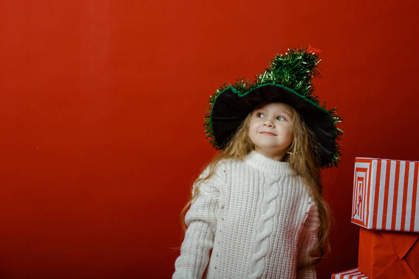 Маленькая милая девочка в студии на красном фоне с рождественскими игрушками - Фото, изображение