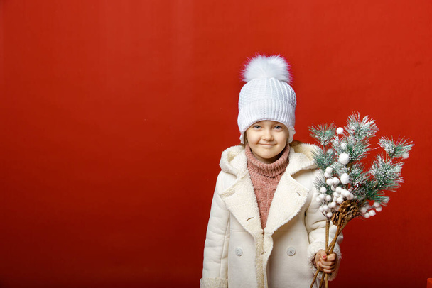 Klein schattig meisje in de studio op een rode achtergrond met kerst speelgoed - Foto, afbeelding
