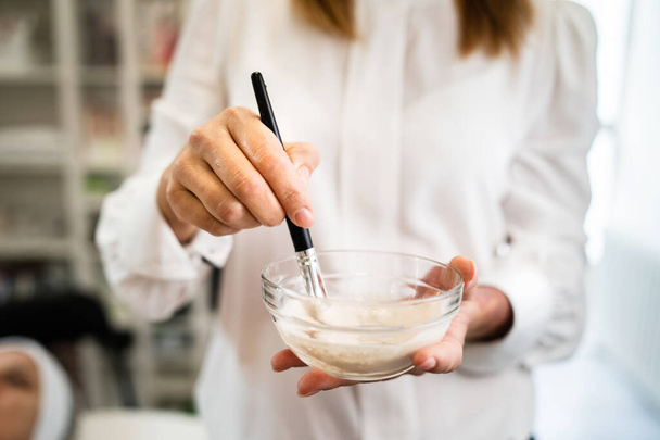 Nahaufnahme der Hände einer Kosmetikerin Kosmetikerin bei der Vorbereitung einer Schönheitsmaskenbehandlung im Wellness-Salon - Mittelteil von vorne mit Kopierraum - Foto, Bild