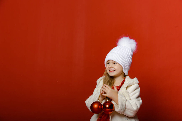 Little cute girl in the studio on a red background with Christmas toys - Photo, Image