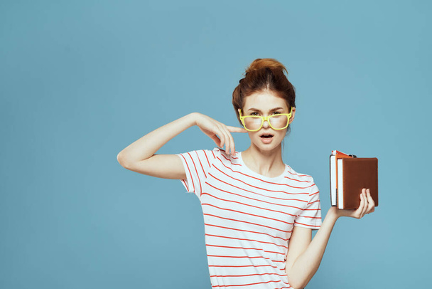 Γυναίκα φοιτητής με βιβλία στα χέρια σε μπλε φόντο και κίτρινα γυαλιά μοντέλο hairstyle περικοπή άποψη - Φωτογραφία, εικόνα