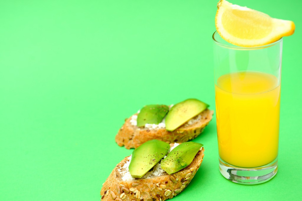 Egészséges avokádó snack és egy pohár narancslé zöld alapon - Fotó, kép