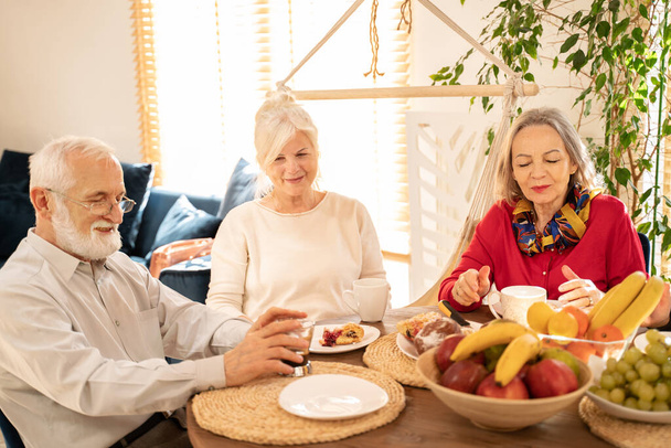Grupo de personas mayores comiendo postre durante una reunión en casa, hablando. Concepto de jubilación feliz. - Foto, imagen