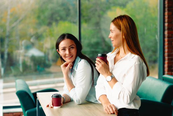 コーヒー休憩。ビジネスの女性は大きな窓のある大きな近代的なオフィスでコーヒーを飲む。彼らは会議の開始を待っていて、ビジネス上の決定をしています. - 写真・画像