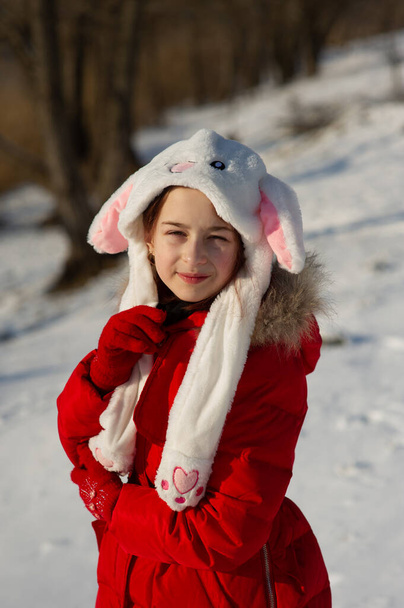 Dziewczynka w pięknym ciepłym czerwonym stroju bawiąca się na zewnątrz w śniegu. Dziewczyna w czerwonej kurtce na ulicy w zimie. Dziewczyna w wieku szkolnym 9 lub 10 lat w zimie. - Zdjęcie, obraz