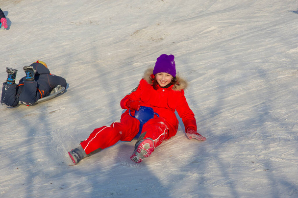 Μικρό κοριτσάκι σε όμορφο ζεστό κόκκινο ντύσιμο παίζει σε εξωτερικούς χώρους στο χιόνι. Κορίτσι με κόκκινο μπουφάν στο δρόμο το χειμώνα. Ένα κορίτσι σχολικής ηλικίας 9 ή 10 ετών το χειμώνα. - Φωτογραφία, εικόνα