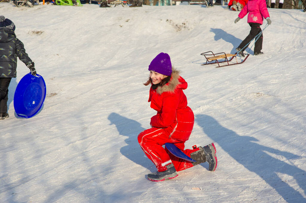Kleine peuter meisje in mooie warme rode outfit spelen buiten in de sneeuw. Meisje in een rode jas op straat in de winter. Een schoolmeisje van 9 of 10 jaar in de winter. - Foto, afbeelding