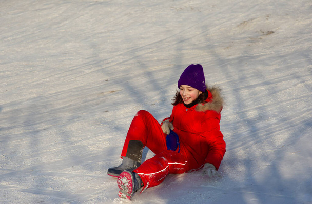 Μικρό κοριτσάκι σε όμορφο ζεστό κόκκινο ντύσιμο παίζει σε εξωτερικούς χώρους στο χιόνι. Κορίτσι με κόκκινο μπουφάν στο δρόμο το χειμώνα. Ένα κορίτσι σχολικής ηλικίας 9 ή 10 ετών το χειμώνα. - Φωτογραφία, εικόνα