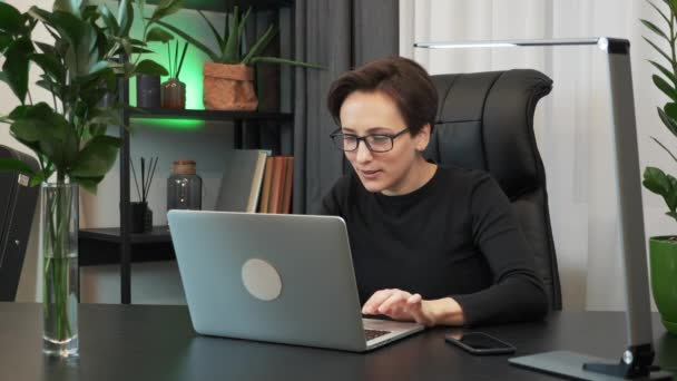 Joyful woman is reading good news on laptop computer. Surprised businesswoman is celebrating victory in office. Happy businesswoman is enjoying success at work - Záběry, video