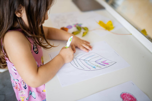 klein meisje kleuren een groot blad afbeelding op een papier vel met een pen - Foto, afbeelding