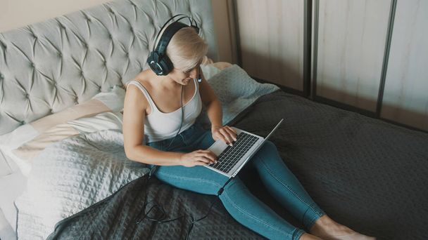Mladá žena používá notebook ve své ložnici. Na volné noze pracuje z pohodlí svého domova - Fotografie, Obrázek