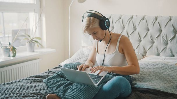 Jeune femme utilisant un ordinateur portable dans sa chambre. Indépendante travaillant dans le confort de sa maison - Photo, image