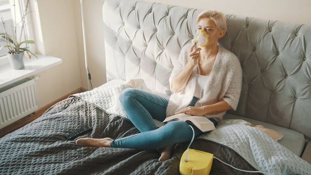 Молода блондинка використовує інгалятор або респіраторну маску в її спальні
 - Фото, зображення