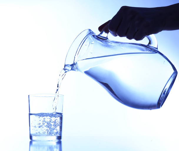 Pouring water into glass on blue background - Photo, Image
