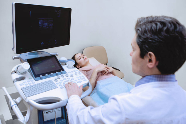 足の超音波検査.医者は若い女性の血管をスキャンします。カウチ、モニターと信号センサーを備えた近代的な装置、医療クリニック. - 写真・画像