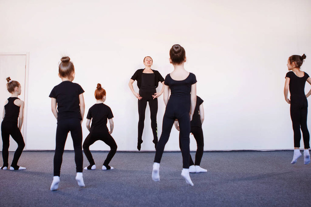 Valmentaja näyttää, miten Entrechat tehdään. Teini tytöt musta trikoot tanssi, baletti tai rytminen voimistelu oppitunti. - Valokuva, kuva