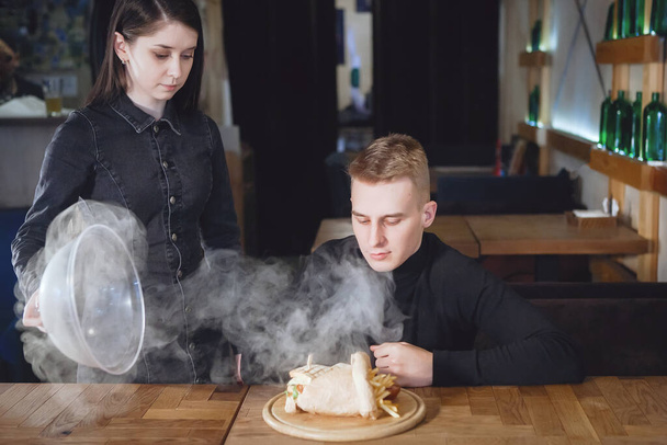 Female waiter serving dishes with smoke to a client in a restaurant. - Photo, Image