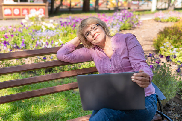 A woman in a Park with a laptop. A middle-aged woman in a Park communicates online - Фото, изображение