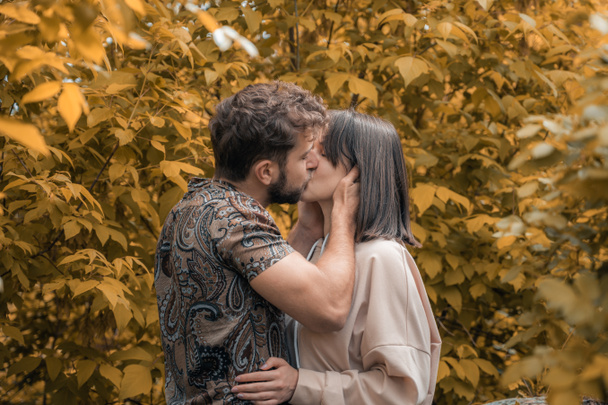 Lovely felt in love sensitive couple of millennial people kissing each other in park. Moody natural skin tone, vivid autumn leaves. Young man and woman tenderly care of each other. Beautiful emotional - Foto, imagen
