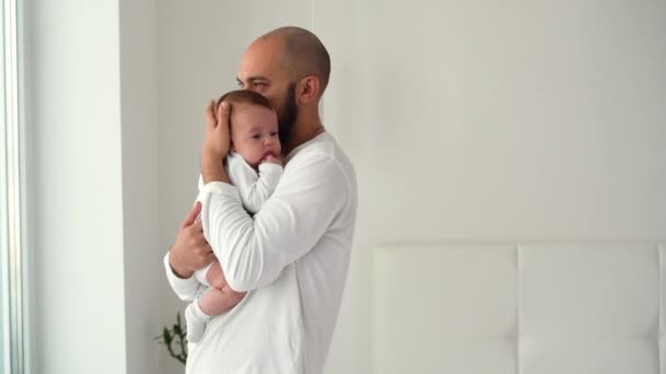 un hombre feliz está en la habitación sosteniendo a un bebé recién nacido en sus brazos y lo abraza. Concepto de padres felices - Metraje, vídeo