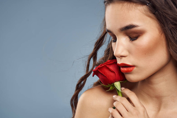 顔の近くに赤いバラを持つ女性の肖像画灰色の背景とメイク巻き毛 - 写真・画像
