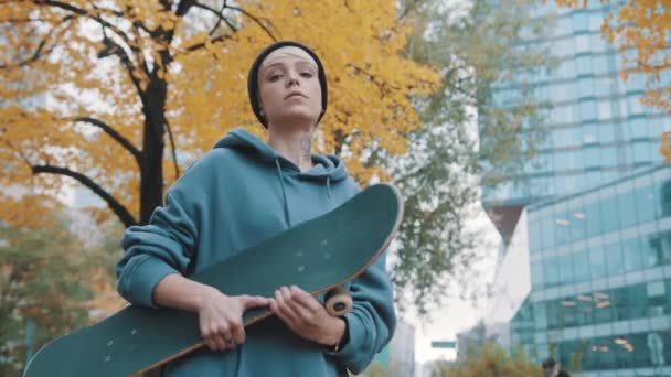 rebelde joven caucásica con monopatín asintiendo su cabeza como aprobación en el parque de la ciudad en otoño - Metraje, vídeo